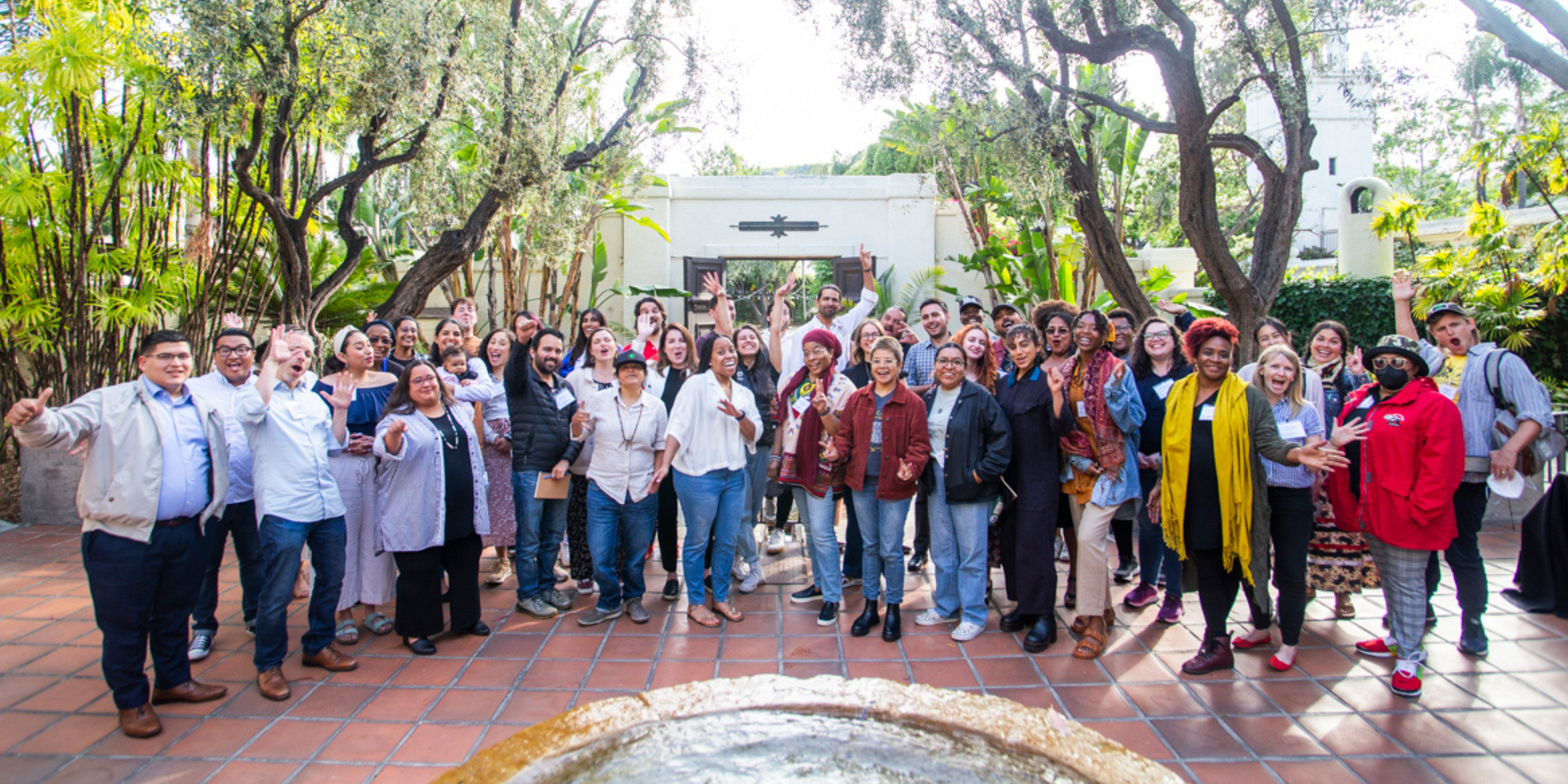 Group of 60 Water Equity and Climate Resilience Caucus members at Los Angeles in person convening smiling with arms raised for posed photo.