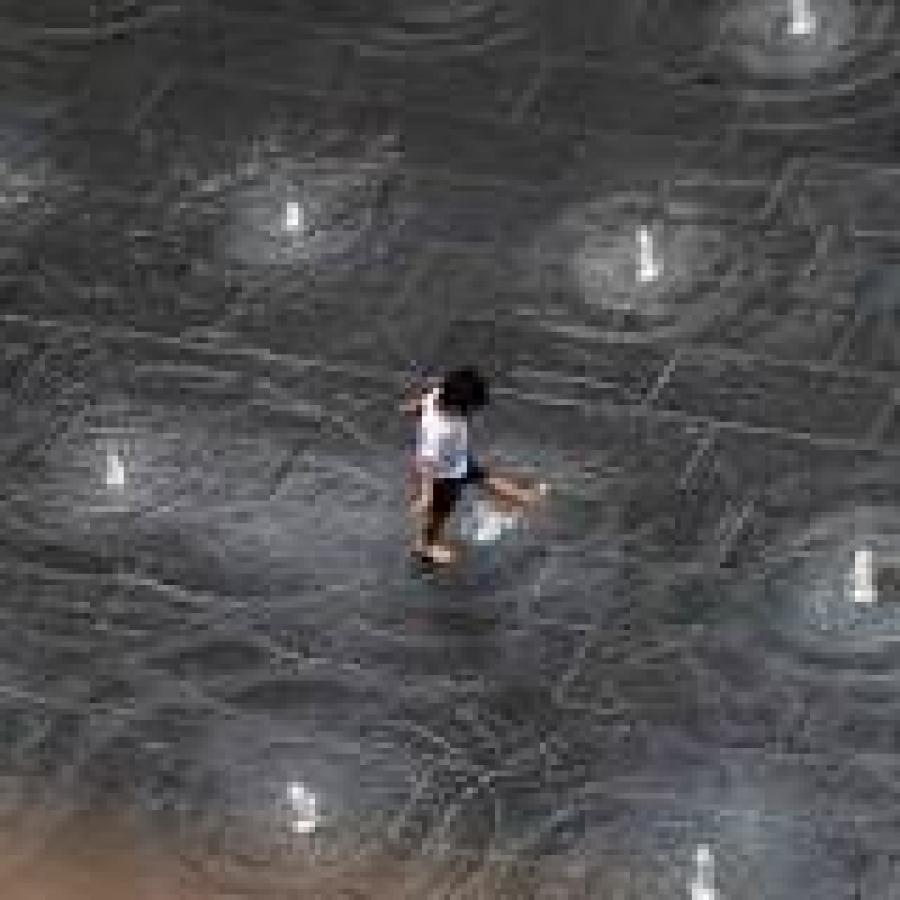 Photograph taken from above of a child playing in a splash pad water fountain.